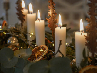 Christmas decoration inspiration. Candles on the table. Table arrangement and setting. Green moss, eucalyptus and dried oranges. Candle holders. Burning flames. Christmas celebration and interior.