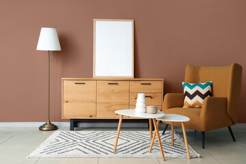 Interior of modern room with comfortable armchair, coffee tables and blank frame on commode near blue wall