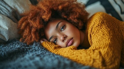 Young woman lies on a bed, resting her chin on her hand and enjoying a quiet moment indoors