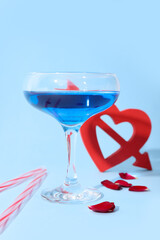 Glass of tasty cocktail with straws and rose petals on blue background. Valentine's Day celebration