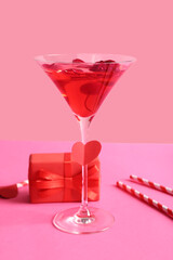 Glass of tasty cocktail with straws and gift on pink background. Valentine's Day celebration