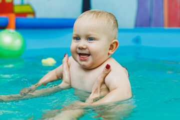 A child swims with his mother in a children's pool. A mother teaches her little son to swim.