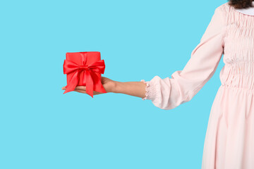 Beautiful young woman with gift box on blue background. Valentine's Day celebration