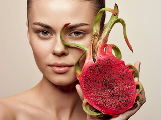 Closeup portrait of a beautiful young woman with dragon fruit slices on her face, on beige...