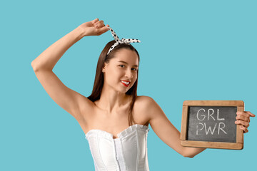 Portrait of young pin-up woman holding chalkboard with text GRL PWR on blue background. Women's...