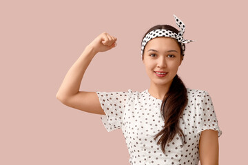 Beautiful young Asian pin-up woman showing her muscles on pink background