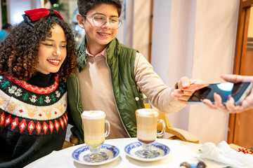 Young latin couple paying contactless in a cafe during christmas time
