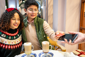 Young latin couple paying christmas cappuccinos by contactless card in cafe