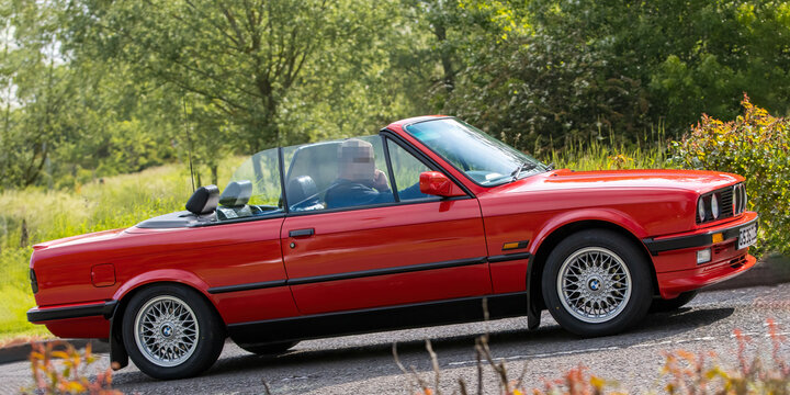 1990 red BMW 3 SERIES 325I CABRIOLET classic car travelling on an English country road.