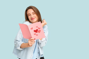 Beautiful young woman holding greeting card with hearts on blue background. Valentine's Day celebration