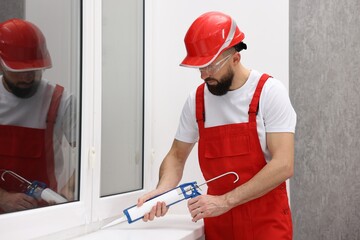 Worker with caulking gun sealing window indoors