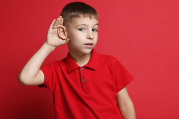 Little boy showing hand to ear gesture on red background