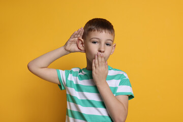 Little boy showing hand to ear gesture on orange background