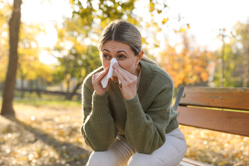 Woman with runny nose on wooden bench in park