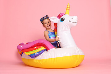 Cute little girl in swimsuit with unicorn pool float on light pink background © New Africa