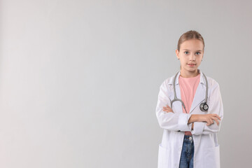 Girl with stethoscope pretending to be doctor on light grey background, space for text. Dreaming of future profession