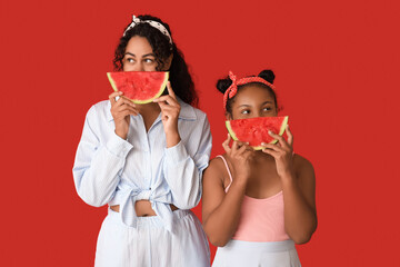 Beautiful young African-American woman and her cute daughter with slices of fresh watermelon on red...