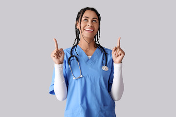 Young African-American female doctor with stethoscope pointing at something on white background