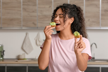African-American woman eating tasty eclair in kitchen