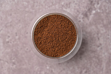 Top view closeup fresh aromatic ground coffee in a small glass on a gray concrete background