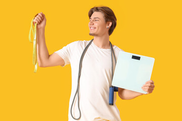 Sporty young man with tape measure and scales on yellow background. Weight loss concept