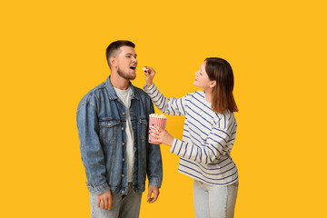 Happy young couple with bucket of popcorn on yellow background
