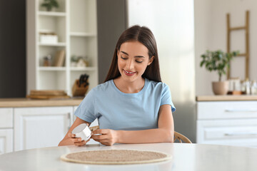 Beautiful young happy woman with wireless portable speaker sitting at table in kitchen