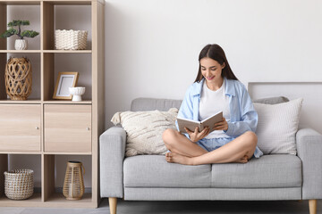 Obraz premium Beautiful young happy woman reading book on sofa at home