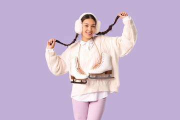 Happy young Asian woman with ice skates on lilac background
