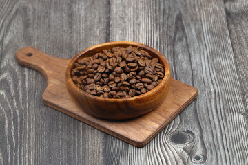 Wooden bowl with coffee beans on wooden background