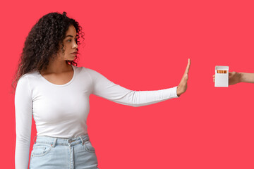 Young African-American woman rejecting pack of cigarettes on red background. Stop smoking concept