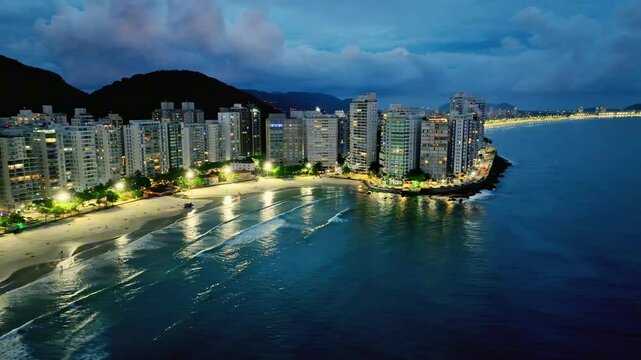 Imagem a&eacute;rea noturna de praia Pitangueiras no Guaruj&aacute; com muitas nuvens de chuva e diversos pr&eacute;dios residenciais usados para loca&ccedil;&atilde;o para temporada.