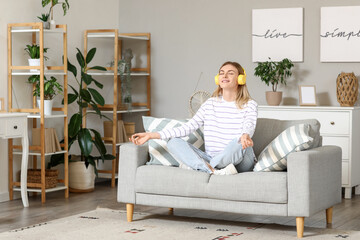 Obraz premium Young woman in headphones meditating on sofa at home