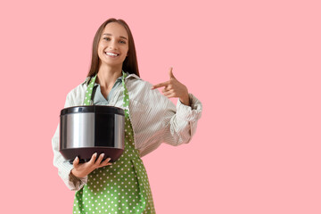 Young housewife pointing at multi cooker on pink background
