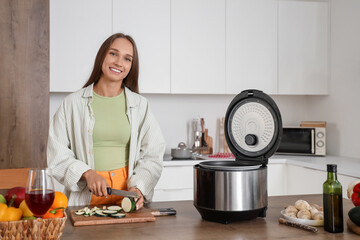 Young woman with multi cooker cutting zucchini at table in kitchen