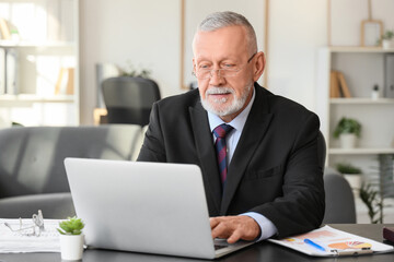 Senior businessman working with laptop at table in office