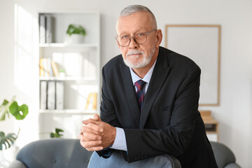 Senior businessman with clasped hands leaning on chair in office