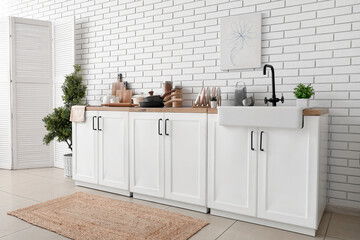 Folding screen and kitchen counter with utensils near white brick wall