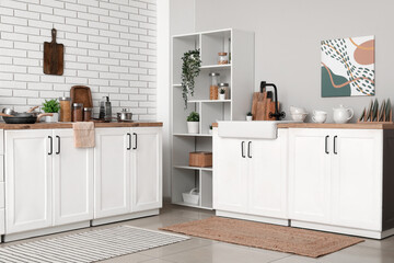 Shelving unit and kitchen counters with utensils in interior of light kitchen