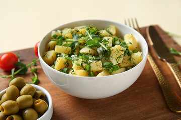 Bowl of tasty potato salad with micro green and olives on yellow background