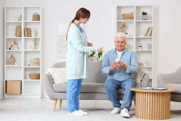 Fototapeta premium Female doctor and mature man with pills sitting on sofa at home