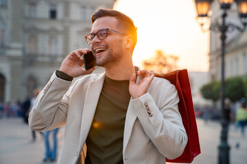 Caucasian professional in business attire speaks on smartphone while carrying shopping bags through...