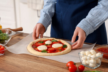 Woman with raw pizza near table in kitchen