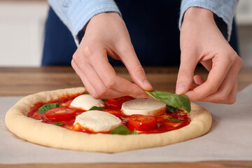 Woman putting basil on dough for pizza near table in kitchen