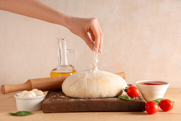 Woman sprinkling raw dough with flour for pizza on wooden table against grunge background
