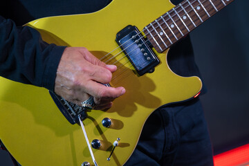 Musician strums yellow electric guitar during live performance, focusing on detailed fingering and...