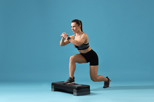 Woman in gym clothes doing exercise with step platform on light blue background