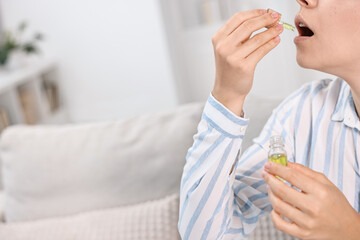 Young woman taking CBD tincture indoors, closeup. Space for text