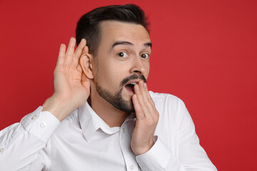 Man showing hand to ear gesture on red background