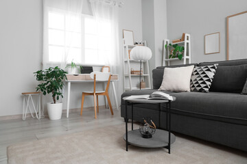 Interior of light living room with black sofa, lamp and workplace